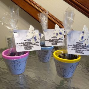 three lavender flower pots on a glass table with dirt in plastic bags and flower seed paper butterflies attached